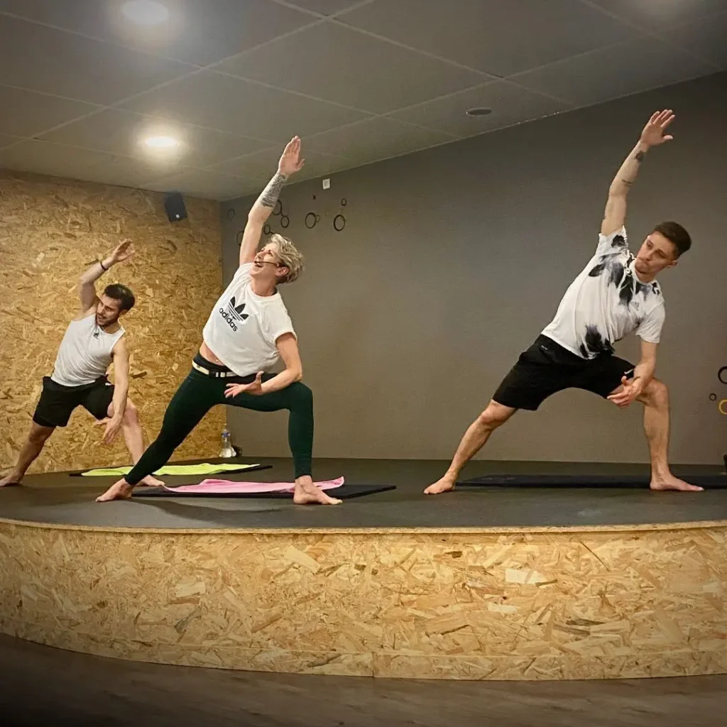 Trois personnes pratiquant le yoga en studio.